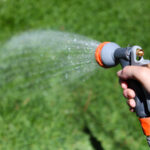 A person watering backyard lawn - sustainable lawn care
